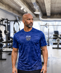 Man wearing RMRL Camo Dry-Fit Performance Tee in Deep Royal Blue camo with gold chest logo in a gym setting