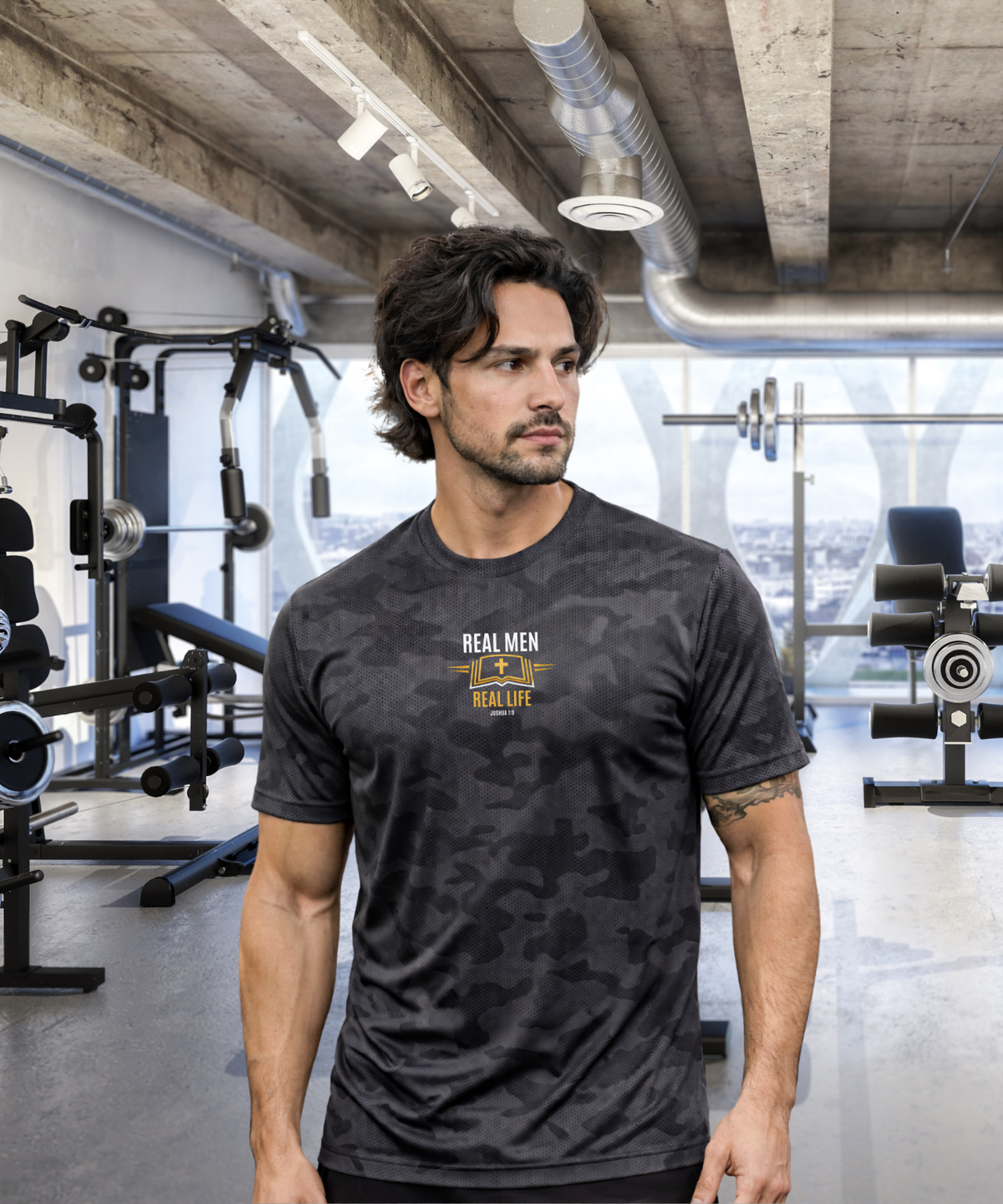 Tattooed man with curly hair in modern gym wearing RMRL Stone Grey Camo Dry-Fit Tee with Real Men Real Life center-chest logo