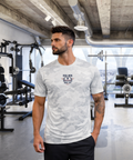 Tattooed man in modern gym wearing RMRL White Camo Dry-Fit Tee with Real Men Real Life left-chest logo