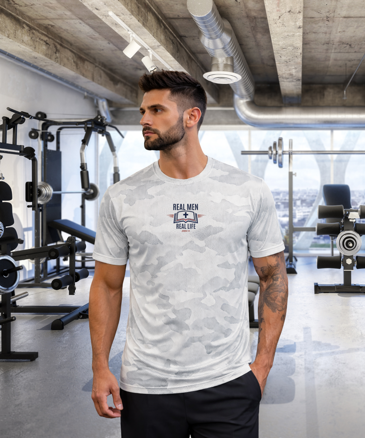 Tattooed man in modern gym wearing RMRL White Camo Dry-Fit Tee with Real Men Real Life left-chest logo