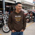 Man wearing RMRL Lifestyle Collection dark chocolate hoodie with gold Real Men Real Life Bible cross graphic outside garage with motorcycles