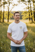 Man in open natural outdoor setting wearing white RMRL Core Identity Collection tee with bold center-chest Real Men Real Life logo